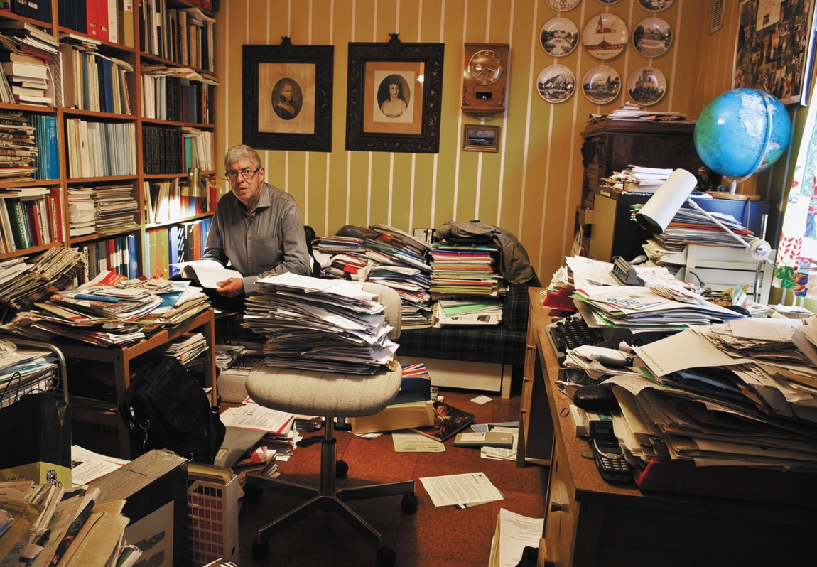 Older adult sitting in an office surrounded by paper stacks before Hazel Park sorting help